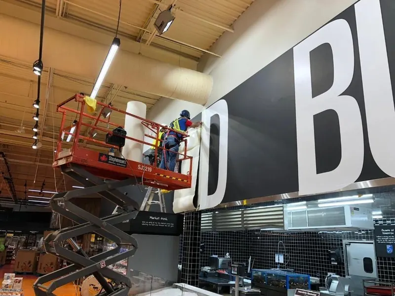 Installers on a lift putting up large wall graphics inside a store