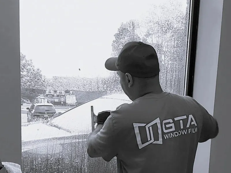 Installer in a GTA Window Film shirt fitting security film to a window